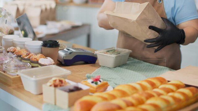 Young asian female customer using mobile phone to pay for paper bag full of freshly baked goods.NFC QR code device,payWave,contactless payment code for fast digital transaction.