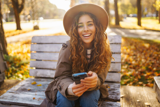Young woman enjoying a sunny autumn day while texting on her smartphone in a park. Concept of vacation, blogging, technology, weekend.
