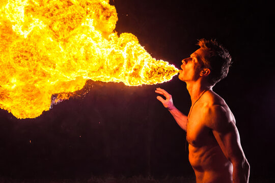 Skilled fire breather dreadlocks night setting performing dangerous flame show, dramatic entertainment art outdoors, breathtaking skill display shirtless performer on dark background