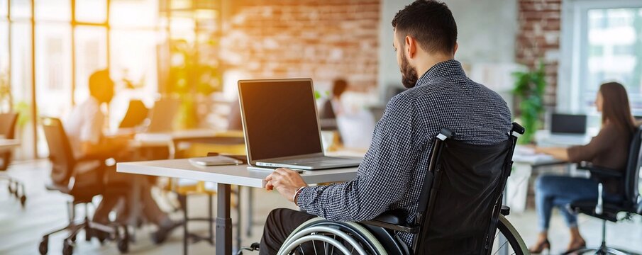 Man in wheelchair working on laptop in modern office.