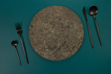 Top view of brown marble plate, black cutlery on dark green background. Food presentation, stone...
