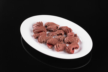 Plate of raw chicken head resting on black background, culinary ingredient or exotic cuisine element, detailed close-up shot.