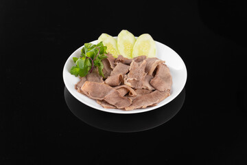 Plate of sliced beef with boiled potatoes and fresh parsley garnish on black background, close-up.