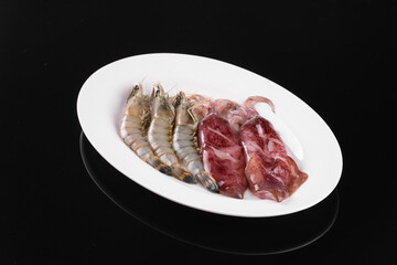 Raw shrimps and steak arranged on a white plate against a black background, perfect for culinary presentations and food blogs.