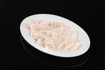 White ceramic plate with thinly sliced raw pork stomach on a black reflective surface, ready for cooking or culinary preparation.