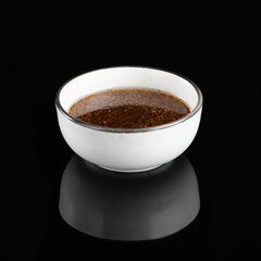 White ceramic bowl filled with a dark liquid, reflecting on a black background. Perfect for food, culinary, and kitchen-themed designs.