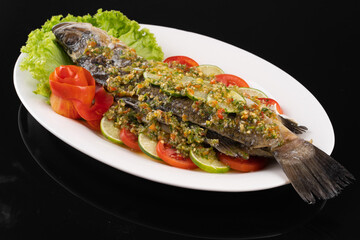 Whole fish garnished with sauce and fresh vegetables on a white plate. Perfect for seafood lovers and culinary presentations.