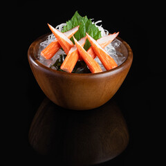 Fresh crab sticks served on ice with garnish in a wooden bowl, beautifully presented on a black background.