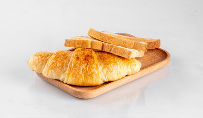 Freshly baked croissant and sliced bread on a wooden tray, perfect for breakfast or a quick snack. Isolated on white background.