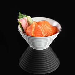 Freshly sliced salmon sashimi served in a white bowl on a black background, showcasing an exquisite...