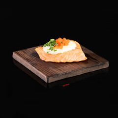 Gourmet appetizer with smoked salmon, cream cheese, and herbs served on a wooden board against a black background.