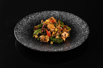 Gourmet dish with vibrant vegetables and succulent meat on a dark speckled plate, set against a black background.