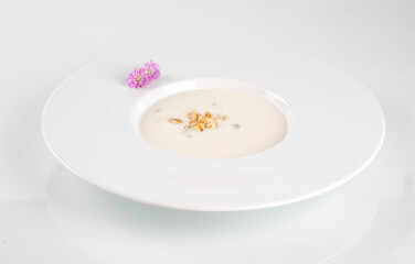 Gourmet mushroom soup in a white bowl, garnished with edible flowers and herbs on a white background. Exquisite presentation.