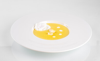 Gourmet pumpkin soup elegantly served with a dollop of cream in a pristine white bowl on a minimalistic background.