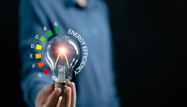 Hand women hold light bulb with energy efficient rating class,  energy saving, net zero, carbon neutrality goals, development business sustainable environmen, energy efficient concept.