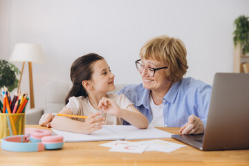 Happy grandma helping adorable preschool granddaughter school kid with homework task. Positive...