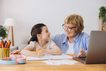 Happy grandma helping adorable preschool granddaughter school kid with homework task. Positive...