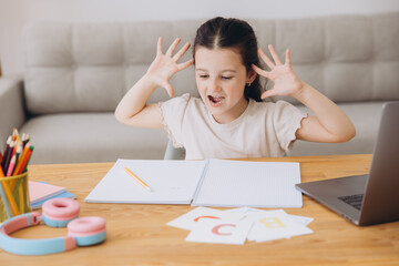 Naklejka premium Remote Study Stress. Sad Little Girl Sitting At Desk With Laptop, Upset Female Child Making Facepalm Gesture, Tired Of Distance