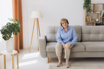 Fototapeta premium Body arthritis muscles stiff problem, aged woman suffering on leg, pain knee from disease chronic, hand massage rubbing joint injury, senior hurt or sore sitting on sofa at home. Health care people.