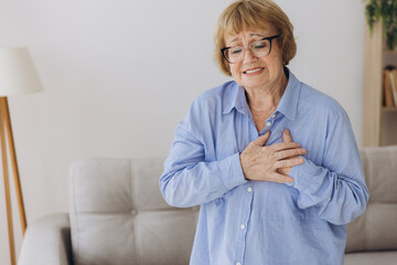 Elderly senior woman feeling heart pain and holding her chest in her living room.