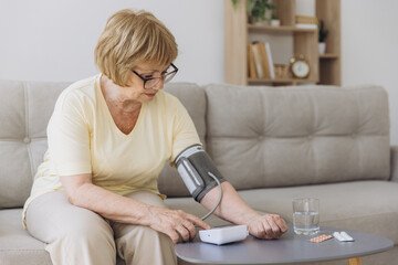 Senior woman with hypertension measuring blood pressure herself at home. Sad Elderly lady measure blood pressure using tonometer. Everyday health check-up