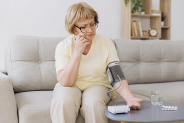 Senior woman with hypertension measuring blood pressure herself at home. Sad Elderly lady measure...