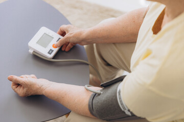 Close-up senior woman with hypertension measuring blood pressure herself at home. Sad Elderly lady measure blood pressure using tonometer.