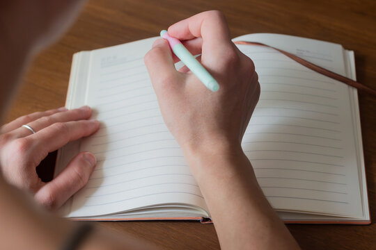 A close-up of a hand holding a pen, poised to write in an open journal. The photo captures the essence of thoughtful planning and personal reflection in a daily diary.