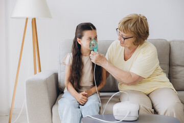 Little girl making inhalation with nebulizer with granny. Woman makes inhalation to a sick child...