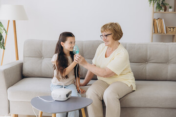 Little girl making inhalation with nebulizer with granny. Woman makes inhalation to a sick child...