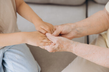 Cropped image of grandmother and granddaughter holding hands each other. Age and generation concept. Family relationship, affection, join, unity.