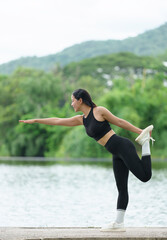 A young Asian woman wearing black exercise clothes, has a good figure, is strong, and is warming up. Stretch your legs before your run in a shady park. Exercise concept for health.