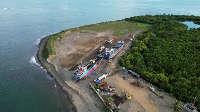Orbiting aerial view of cargo ships stationed on top of land facing tropical shoreline of Catanduanes, Philippines during daytime.