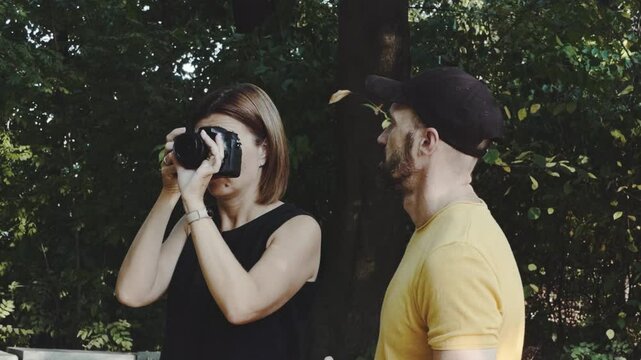 The woman is taking pictures on the camera, and the man is standing next to him and telling something.