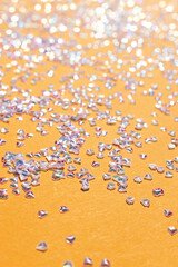 Tiny silver crystal confetti scattered on a yellow background. Selective focus.
