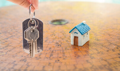 House key in girl hand with miniature house on antique chinese compass over blurred background,...