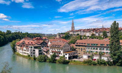 Picturesque view of Bern, Switzerland showcasing the Aare River, historic architecture, and vibrant greenery under a clear blue sky