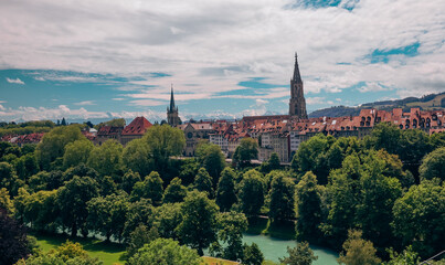 Fototapeta premium A scenic view of Bern, Switzerland showcasing historic architecture and lush greenery along the river on a bright sunny day