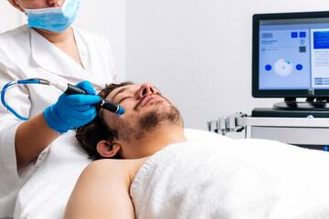 Man receiving a hydrafacial treatment in a modern cosmetic center. Innovative skin hydration and...