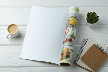 Open magazine with blank page, coffee, plant and notebooks on white wooden table, above view....