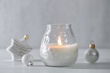 Burning candle and baubles on white wooden table, closeup
