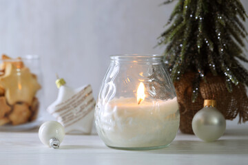 Burning candle and Christmas decor on white wooden table, closeup