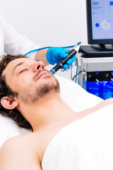 Man receiving a hydrafacial treatment in a modern cosmetic center. Innovative skin hydration and...