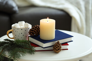 Burning candle, books, fir branches and cones on coffee table indoors. Christmas atmosphere