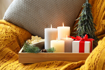 Tray with burning candles and Christmas decor on armchair