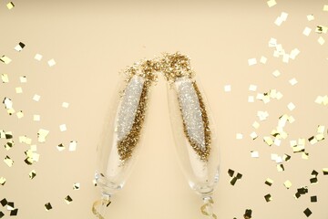Wine glasses with confetti on beige background, flat lay. Christmas decor