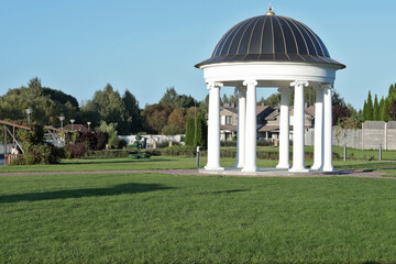 White rotunda in park. Building with columns and roof for holidays. Architectural structures and...