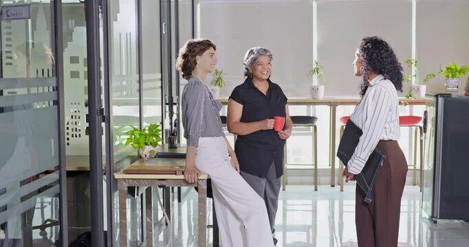 Indian young adult women intern old aged lady hold cup mug drink coffee talk gossip work place expert teen girl staff group team speak idea blab share enjoy fun joy tea break day spend time job office