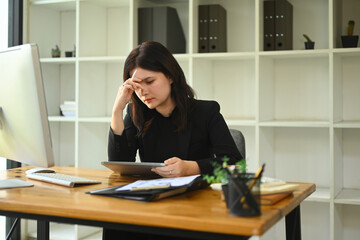 Exhausted young businesswoman sitting at office desk suffering from headache