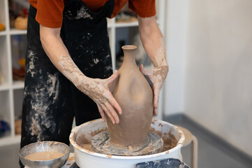 Close-up of a potter's hands making a ceramic vase on a potter's wheel. 